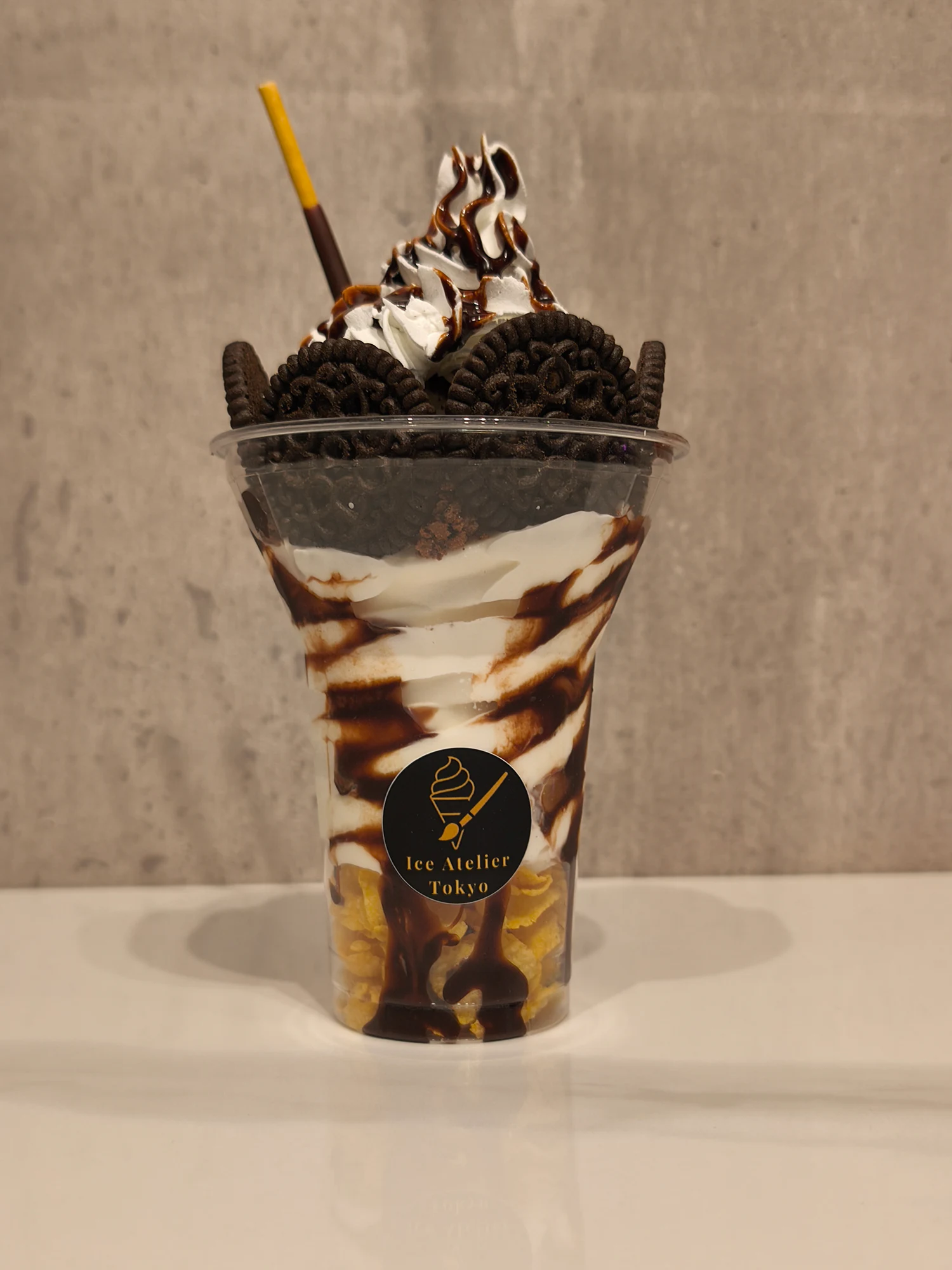 チョコレートソースと黒いクッキーをトッピングした、背の高いICE ATELIER TOKYOの商品